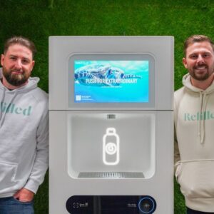 A photo of two men standing with a Refiller drink dispenser between them, against a green background