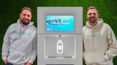 A photo of two men standing with a Refiller drink dispenser between them, against a green background