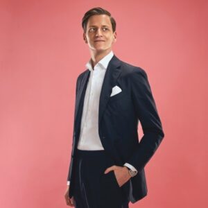 Portrait of etaily founder Alexander Friedhoff wearing a black suit and white shirt against a rose colored background